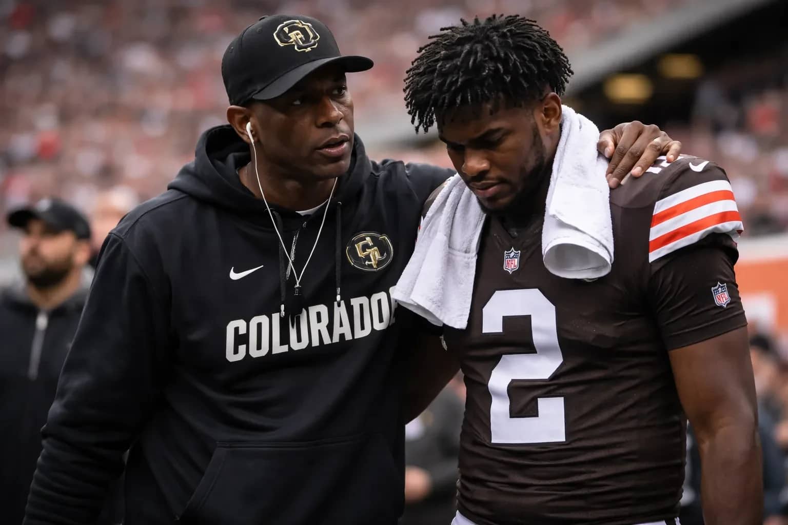 Deion Sanders and Shedeur Sanders standing together on a football field